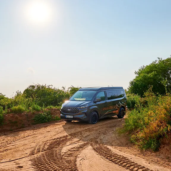 Karmann-Mobil Campingbus fährt auf einer Straße mit weitem Blick über bewaldete Hügel bei stimmungsvollem Sonnenuntergang.